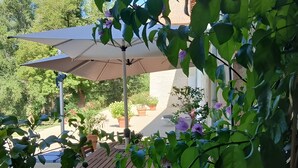 An outdoor patio area with a table and chairs, a large umbrella, and potted plants. - Guest Room “Blue Room” in the Château (Saint-Privat des Prés)