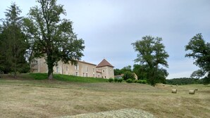 A stone building with a red roof, surrounded by trees and hay bales in a grassy field. - Guest Room “Blue Room” in the Château (Saint-Privat des Prés)