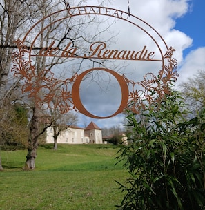 Une plaque métallique portant l’inscription « CHÂTEAU La Renaudie », placée dans un parc, avec un bâtiment visible en arrière-plan.