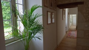A hallway with a potted plant, framed pictures on the wall, and a wooden floor. - Guest Room “Blue Room” in the Château (Saint-Privat des Prés)