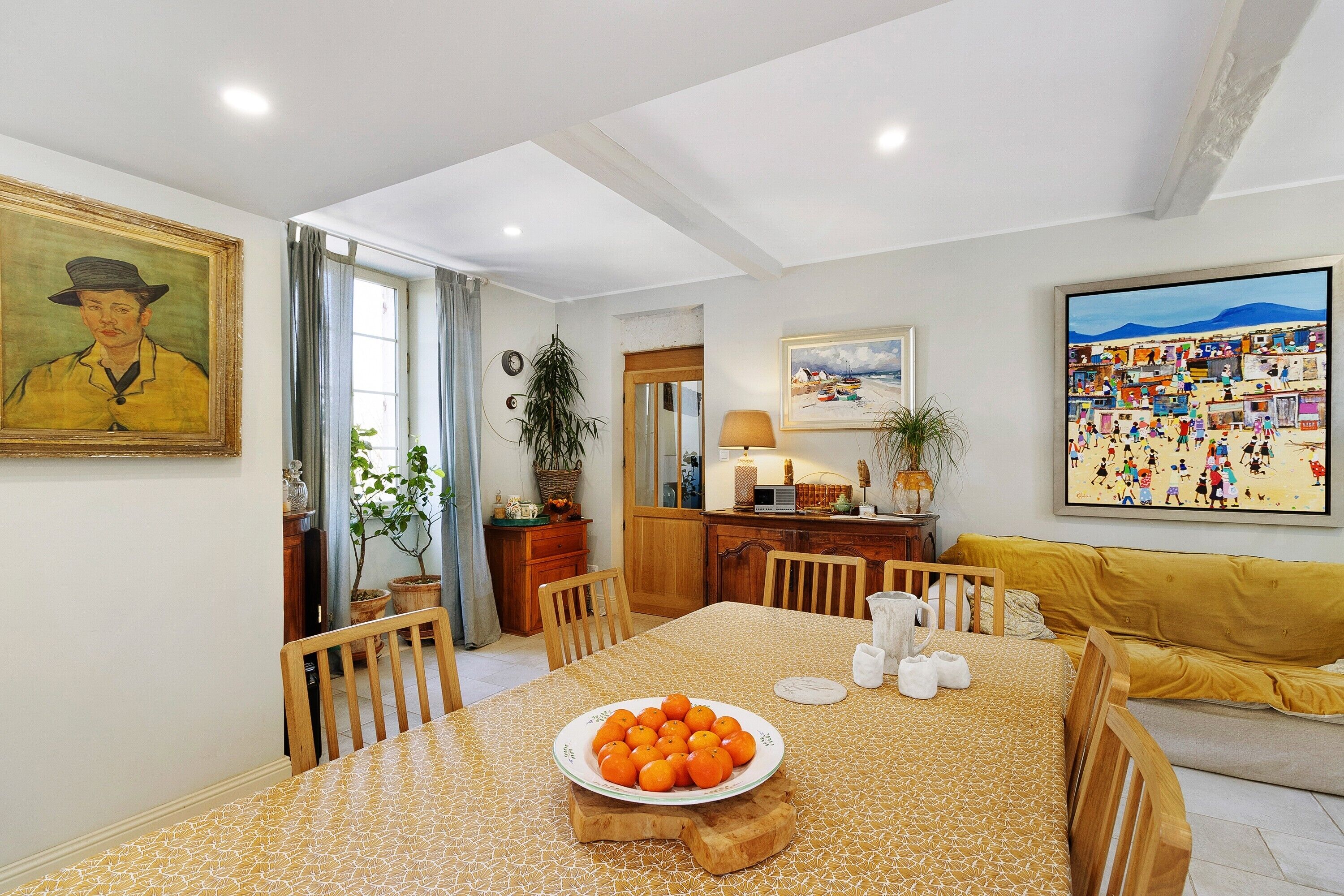 Un comedor con una mesa dispuesta para dos, un plato de naranjas y un cuadro en la pared.