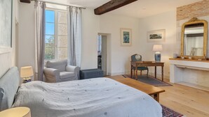 Un dormitorio con cama, una silla, una mesa, un espejo y una chimenea.