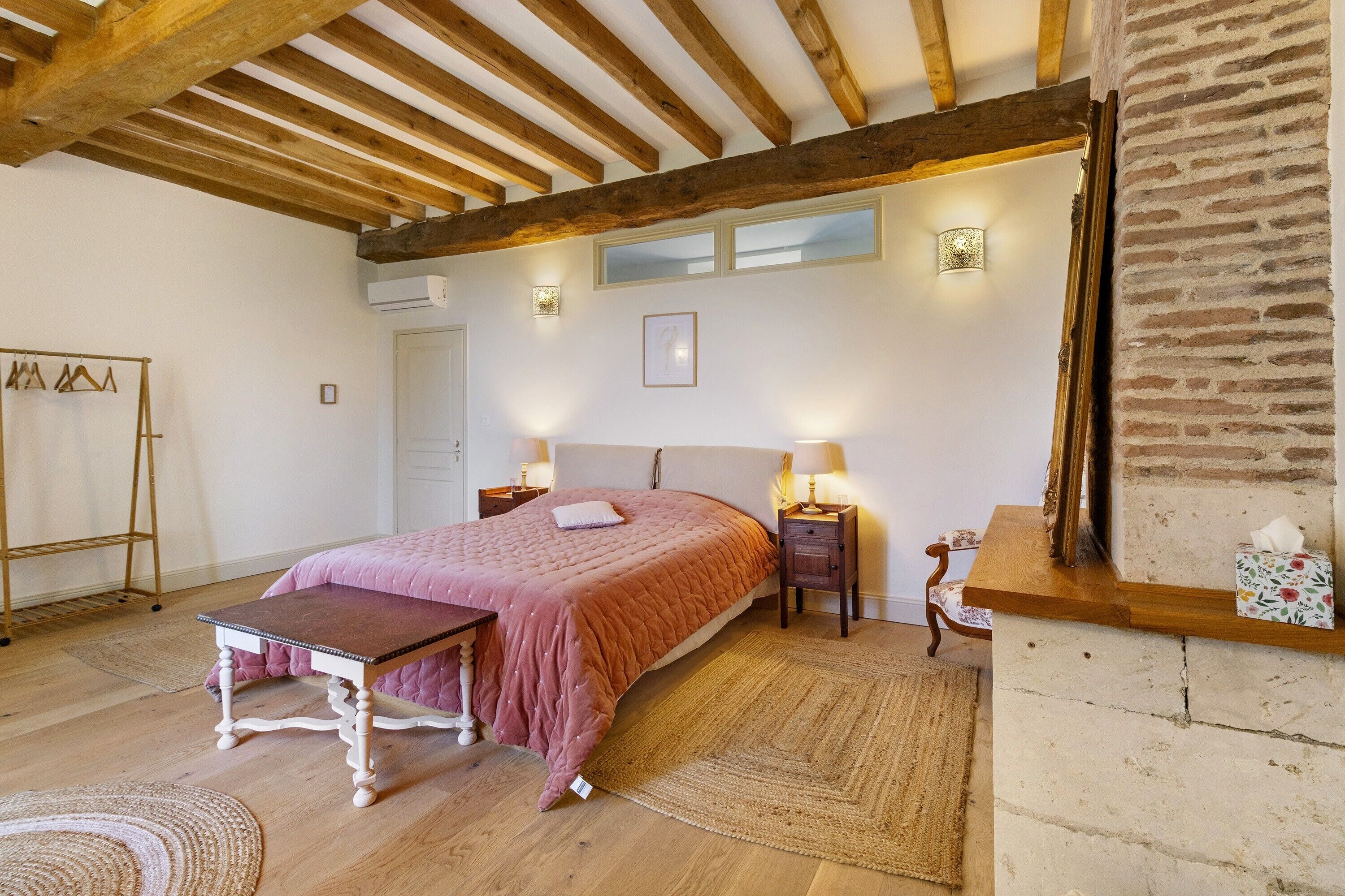 Una camera da letto con un letto, comodini, una panca, un tappeto, una panca in legno e una parete in mattoni.