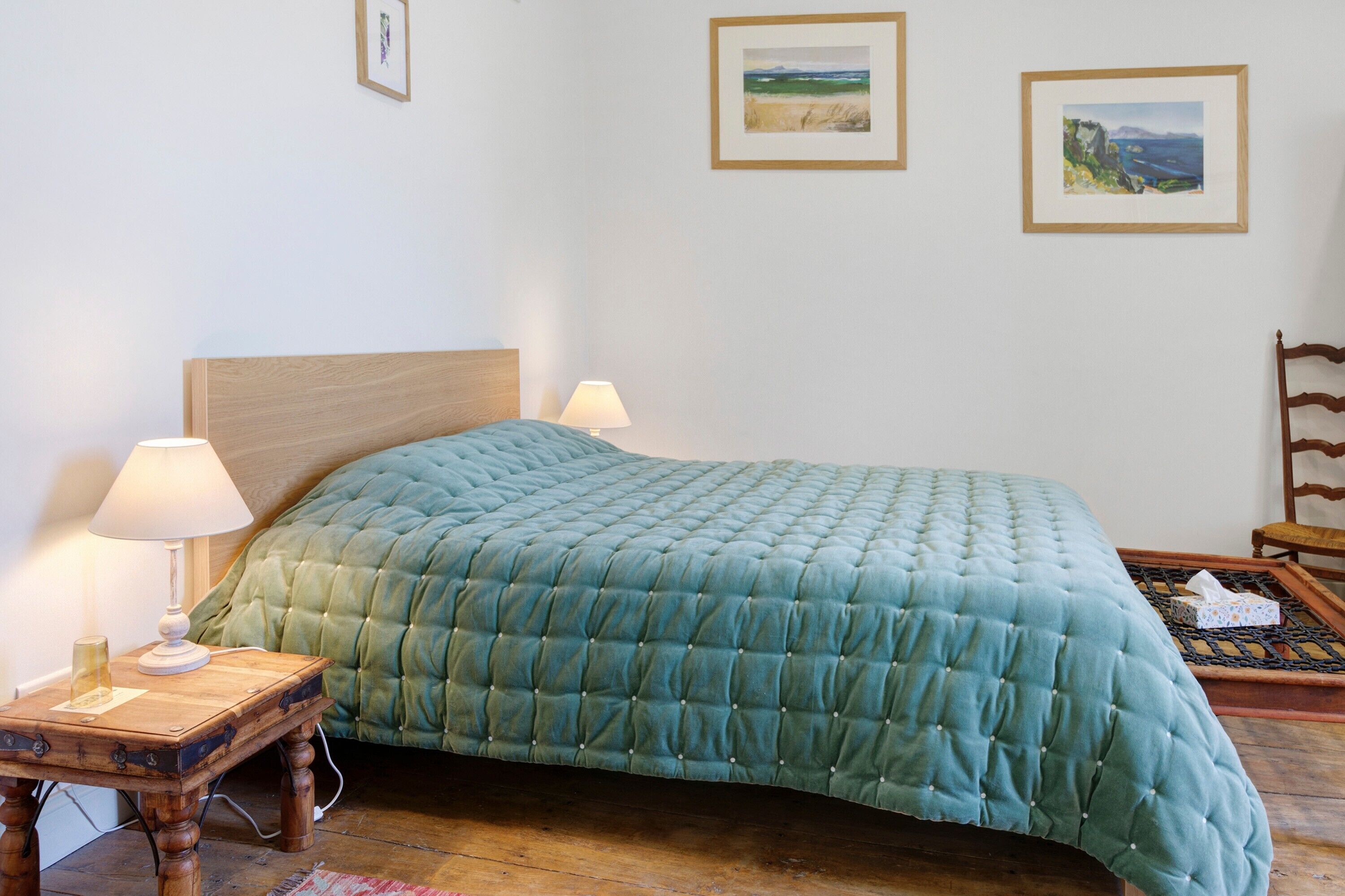 Een slaapkamer met een bed, nachtlampjes, een houten nachtkastje en twee foto's in lijsten aan de muur.