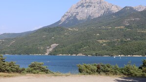 A mountainous landscape with a clear blue lake, a sailboat, and a distant house. - Apartment between lake and mountains, near resort (Chorges)