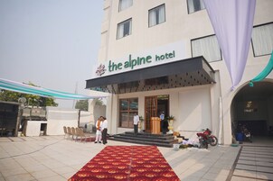 Hotel de montaña con alfombra roja que lleva a la entrada, mesas al aire libre y una motocicleta estacionada afuera.