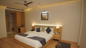 Habitación de hotel con una cama grande, cabecera de madera, lámparas de noche, mesita de noche, una pequeña mesa y un ventilador de techo.