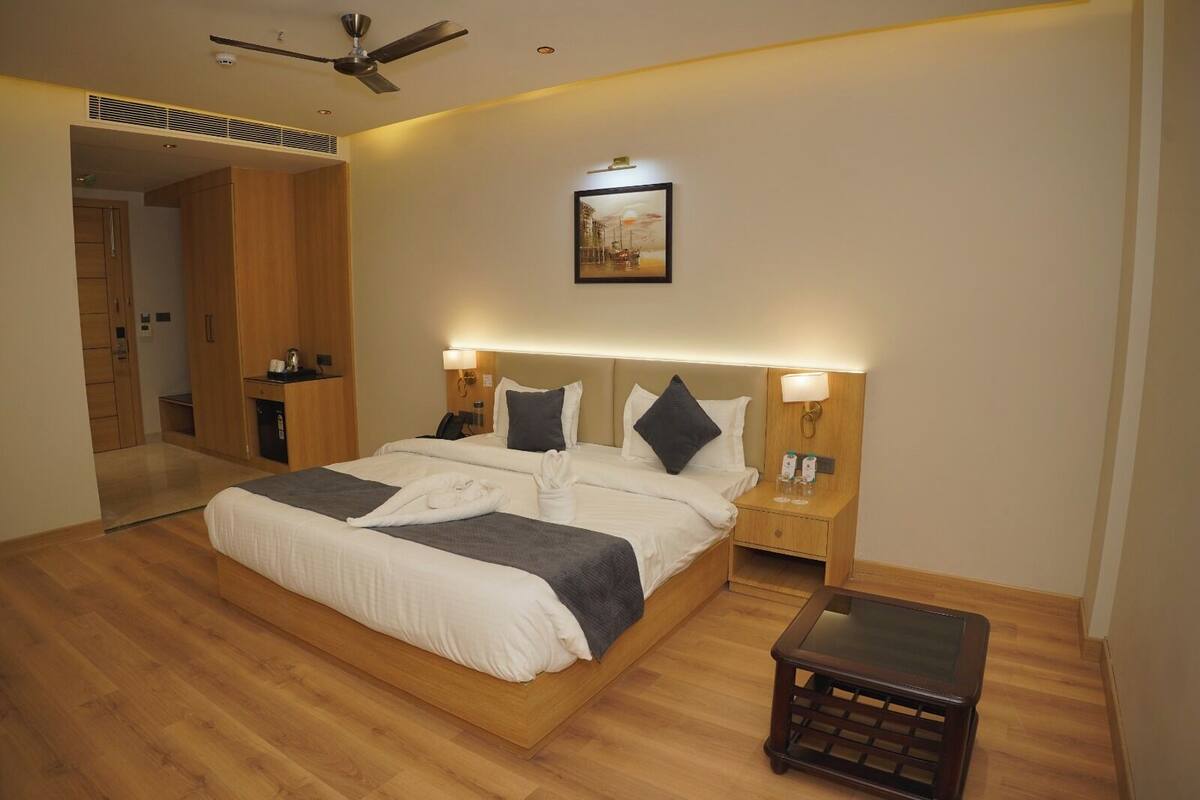 Habitación de hotel con una cama grande, cabecera de madera, lámparas de noche, mesita de noche, una pequeña mesa y un ventilador de techo.