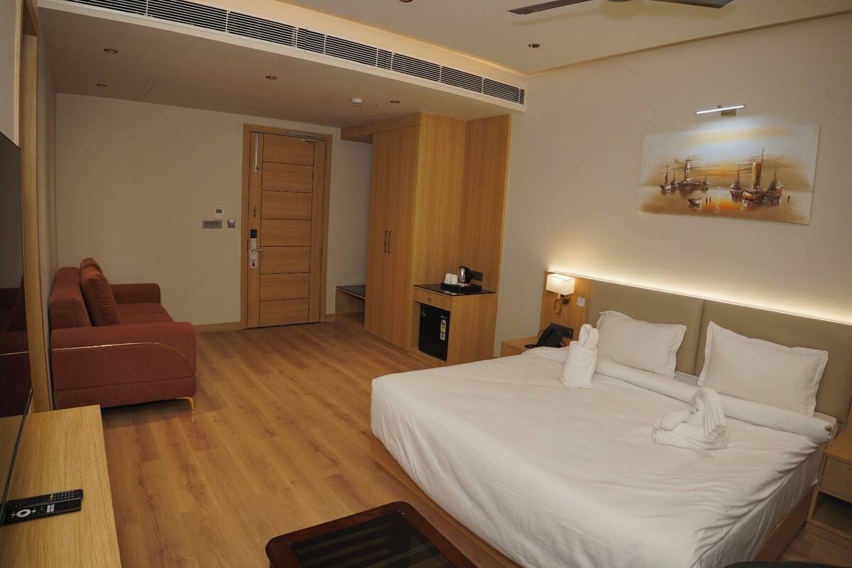 Habitación de hotel con cama, escritorio, silla, armario, un cuadro en la pared y una puerta.