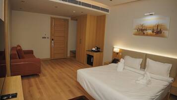 A hotel room with a bed, a desk, a chair, a wardrobe, a painting on the wall, and a door.