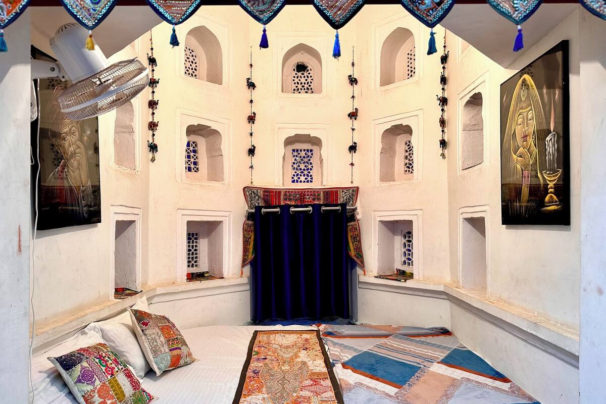 Een kamer met een bed, kussens, een blauw gordijn en een kamerbreed tapijt.