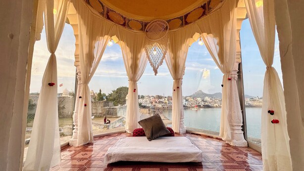 Una habitación con una cama, cortinas blancas y vistas a la ciudad y al agua.