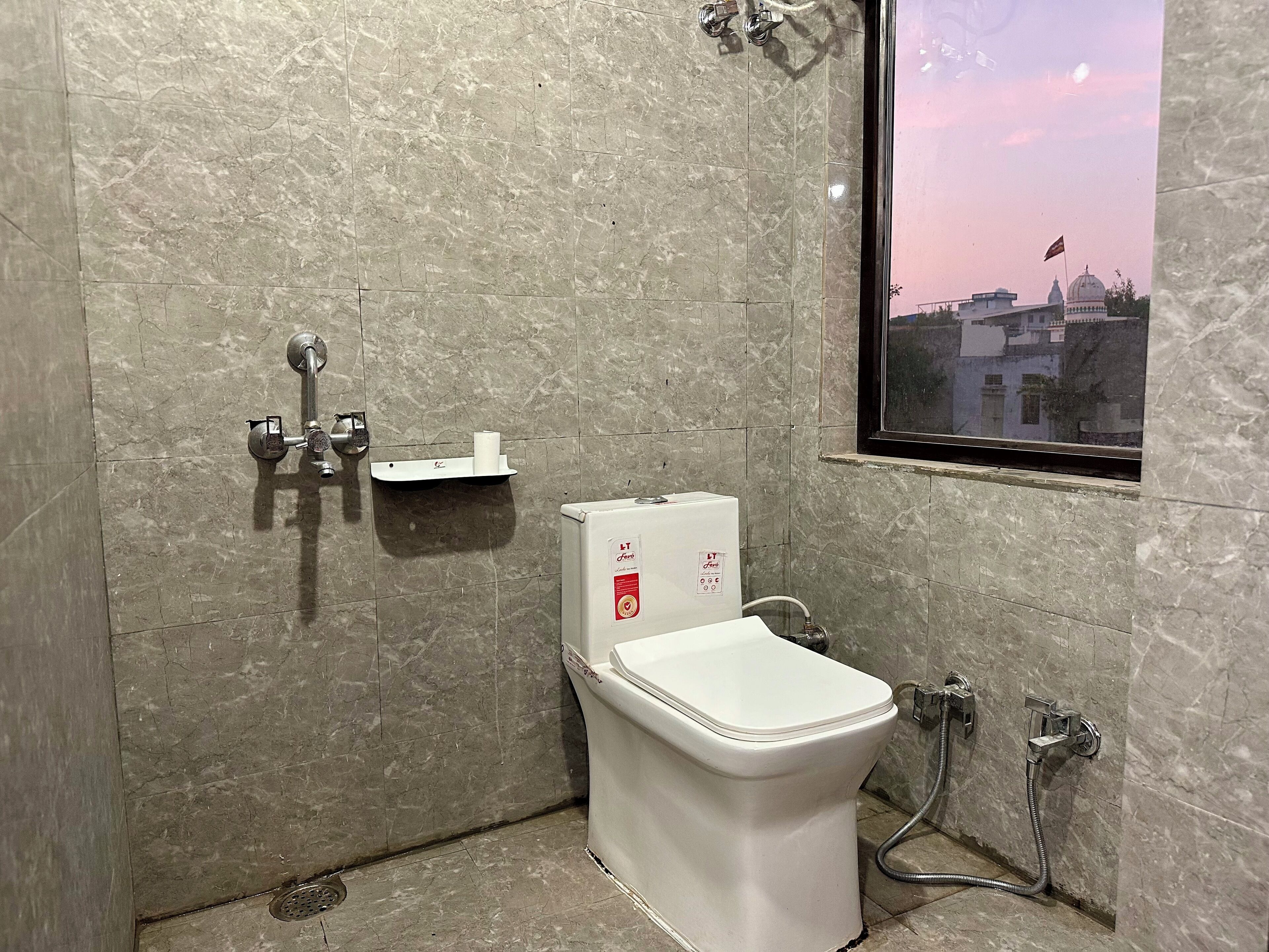 Une salle de bain avec des toilettes, une douche et une fenêtre donnant sur un immeuble.