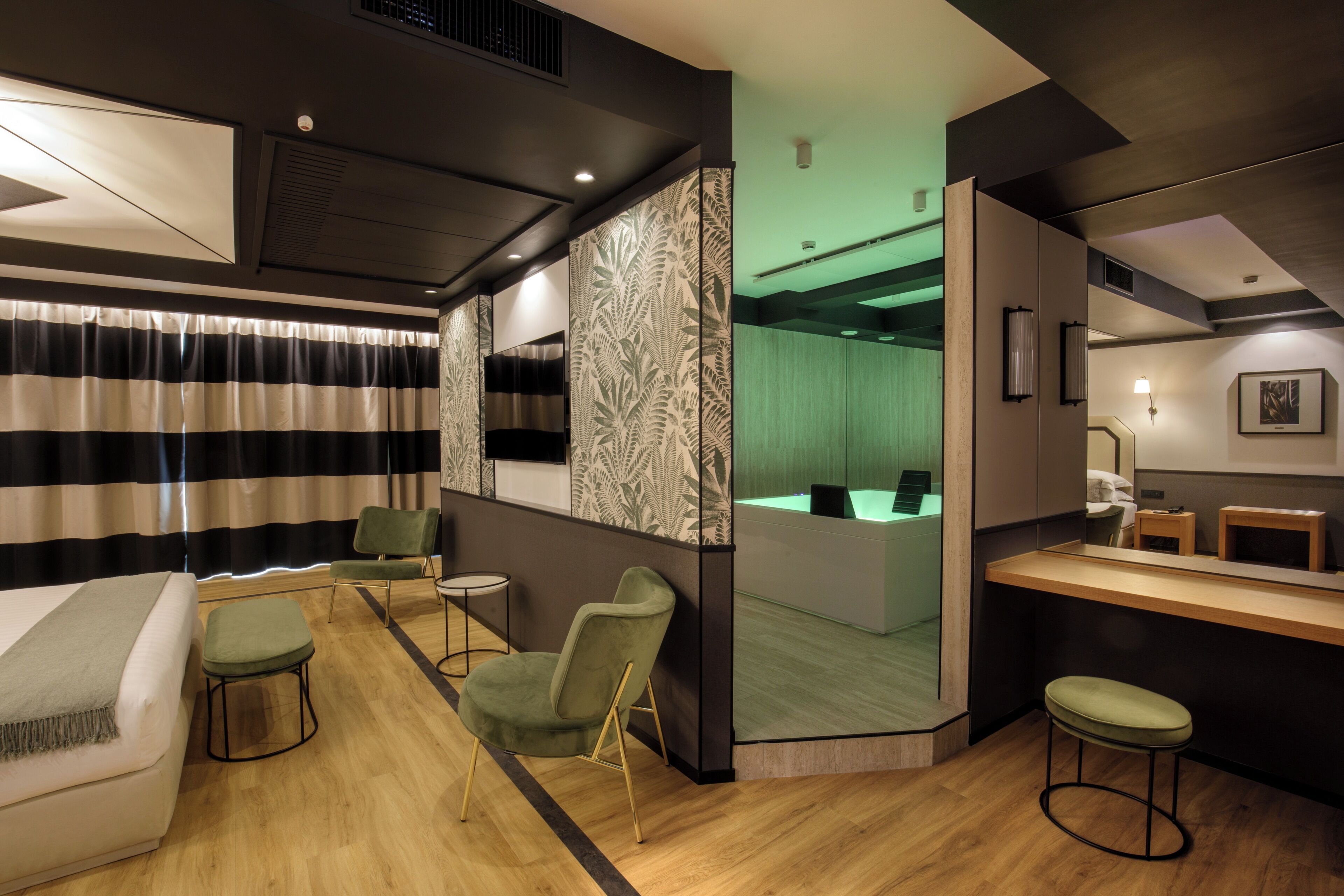 A modern hotel room with a bed, a desk, a chair, a small table, and a bar area.