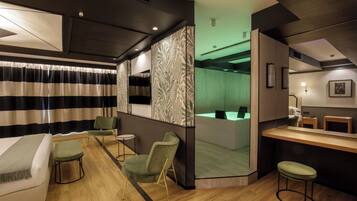 A modern hotel room with a bed, a desk, a chair, a small table, and a bar area.
