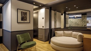 A modern hotel room with a green chair, a round beige sofa, and a large mirror reflecting the room's decor. - The Fourth Dimension by Domidea (Rome)