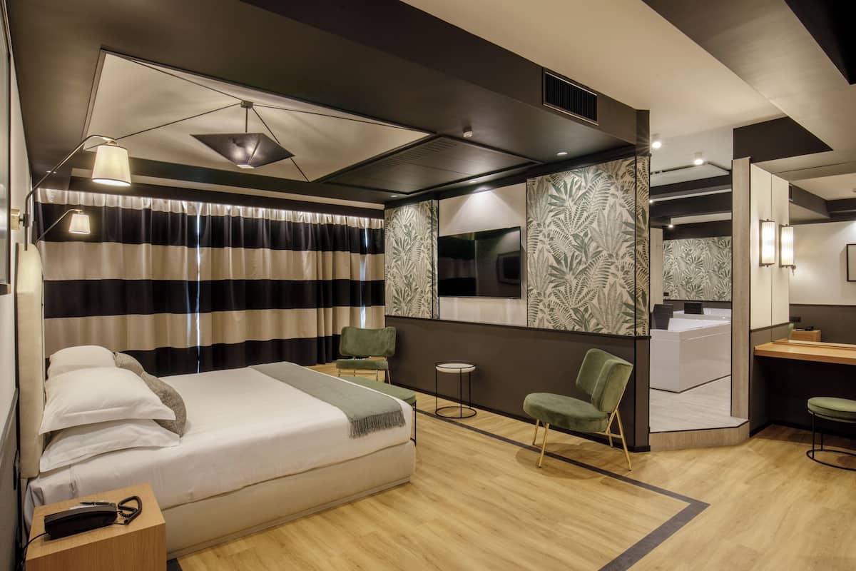 Una habitación de hotel moderna con una cama grande, dos sillas, una mesita y un espejo.
