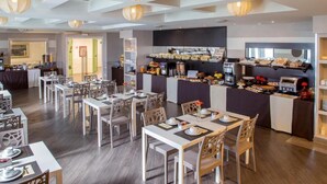 A modern dining area with multiple tables and chairs, a buffet counter with various food items, and a coffee station. - The Fourth Dimension by Domidea (Rome)