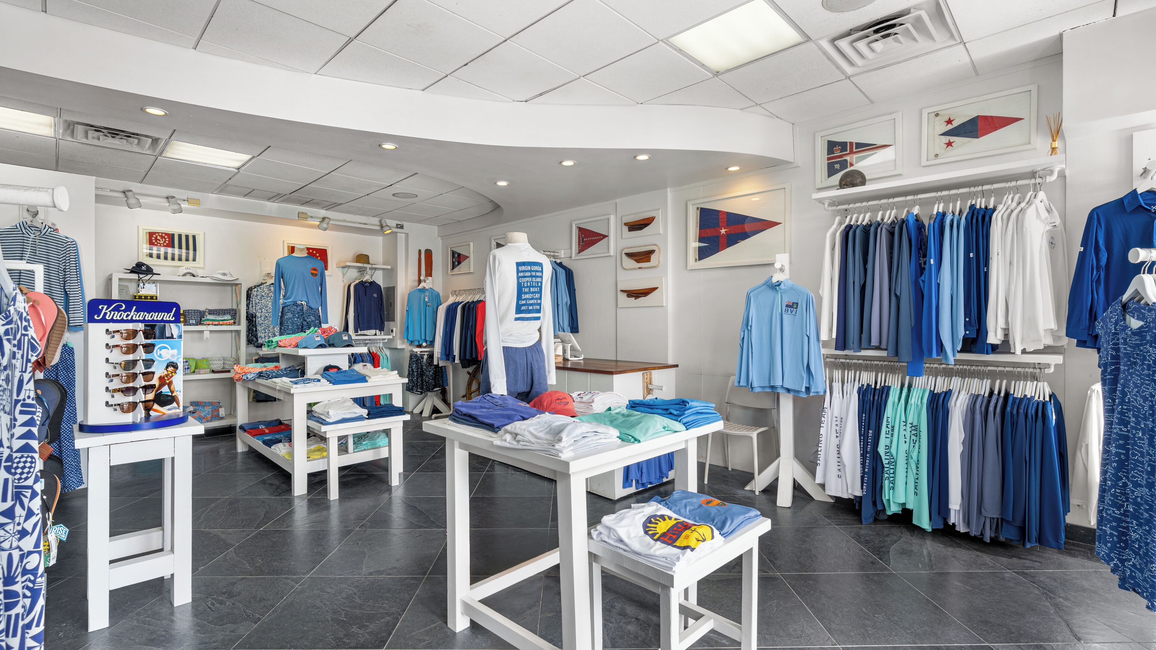 A clothing store with racks of blue and white shirts, a display table with folded clothes, and a sign for 'Knockaround'.