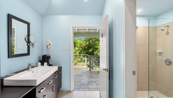 A bathroom with a double sink, a mirror, a hairdryer, and a shower area.