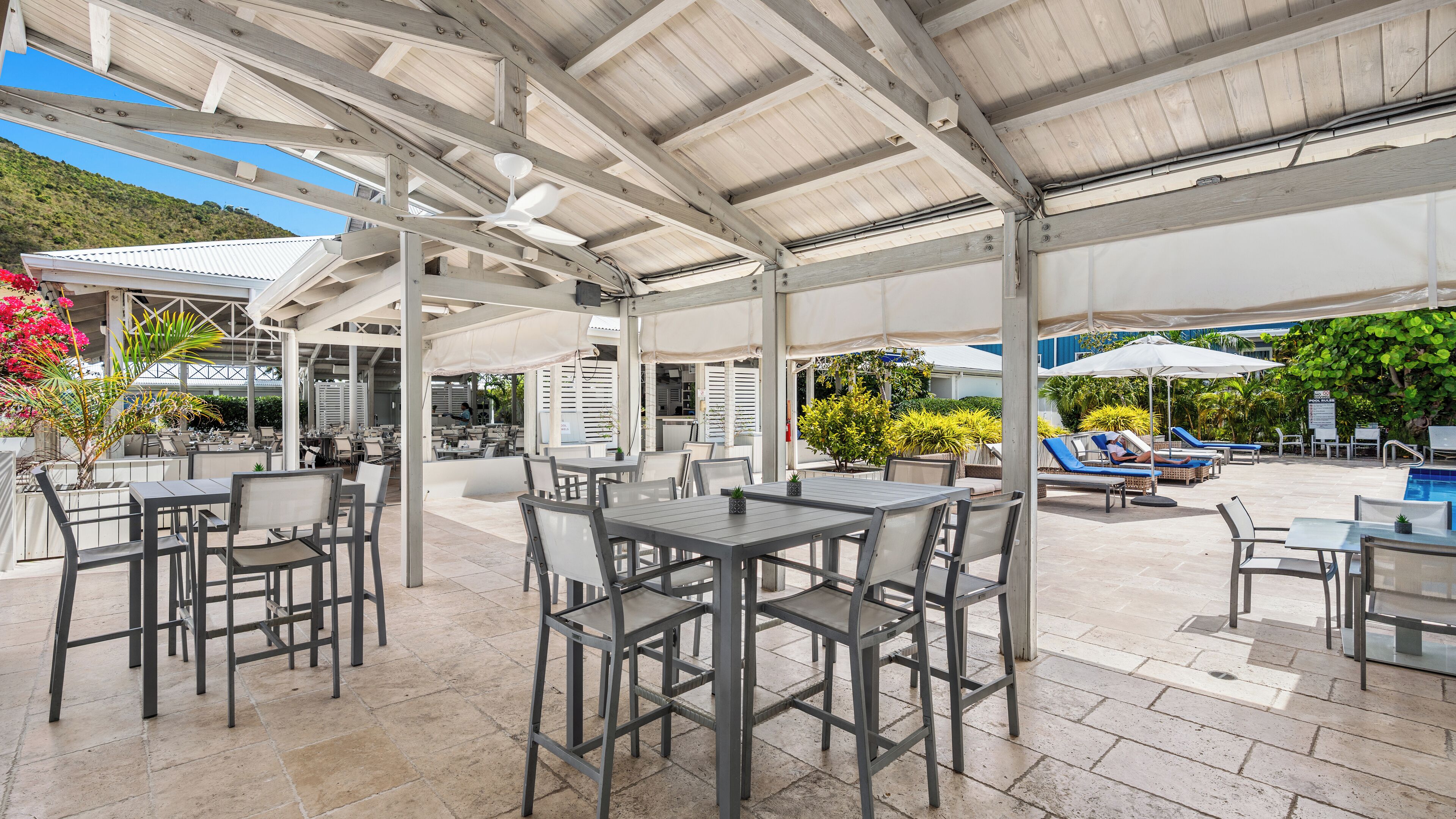 An outdoor patio area with tables and chairs, a pool, and umbrellas.