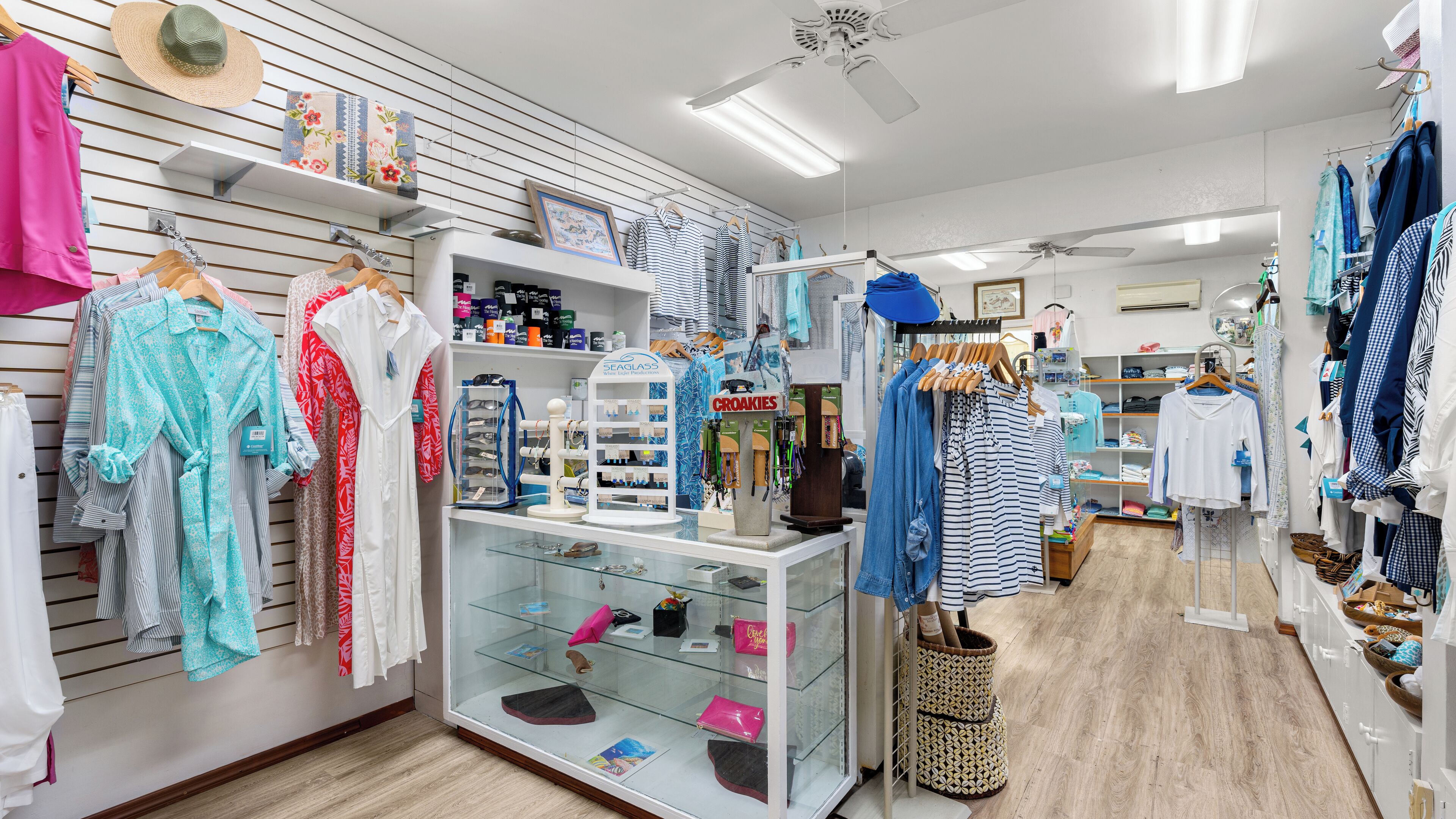 Uma loja de roupas com araras de peças, uma vitrine de sapatos e um espaço para acessórios.