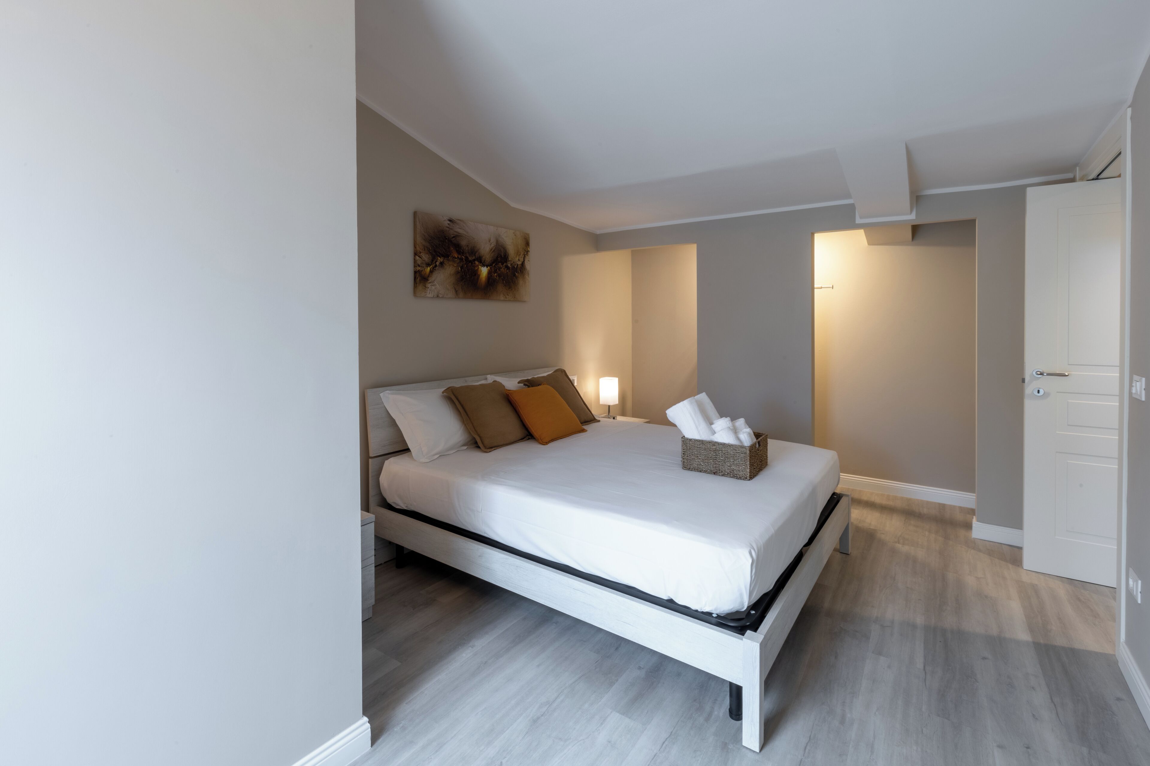 Ein modernes Schlafzimmer mit einem Bett, Nachttischen, einem Wandbild und einer Tür zu einem anderen Raum.