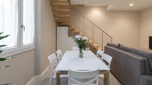 A modern living room with a white dining table, grey sofa, and a staircase with wooden steps. - Orsini 98 Apartments by Mamo Florence (Florence)