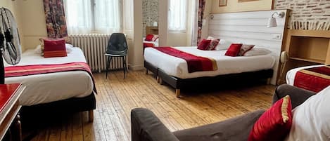 Habitación de hotel con dos camas, suelo de madera, un sofá, una silla, un ventilador de pie y una ventana con cortinas.