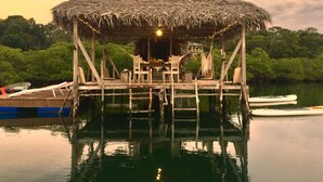 A thatched-roof wooden structure with a table and chairs, surrounded by calm water and greenery. - Lima Limón Eco Island - Panama (Bocas del Toro)