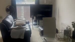 Een woonkamer met een bank, een glazen tafel, een televisie en uitzicht op buiten.