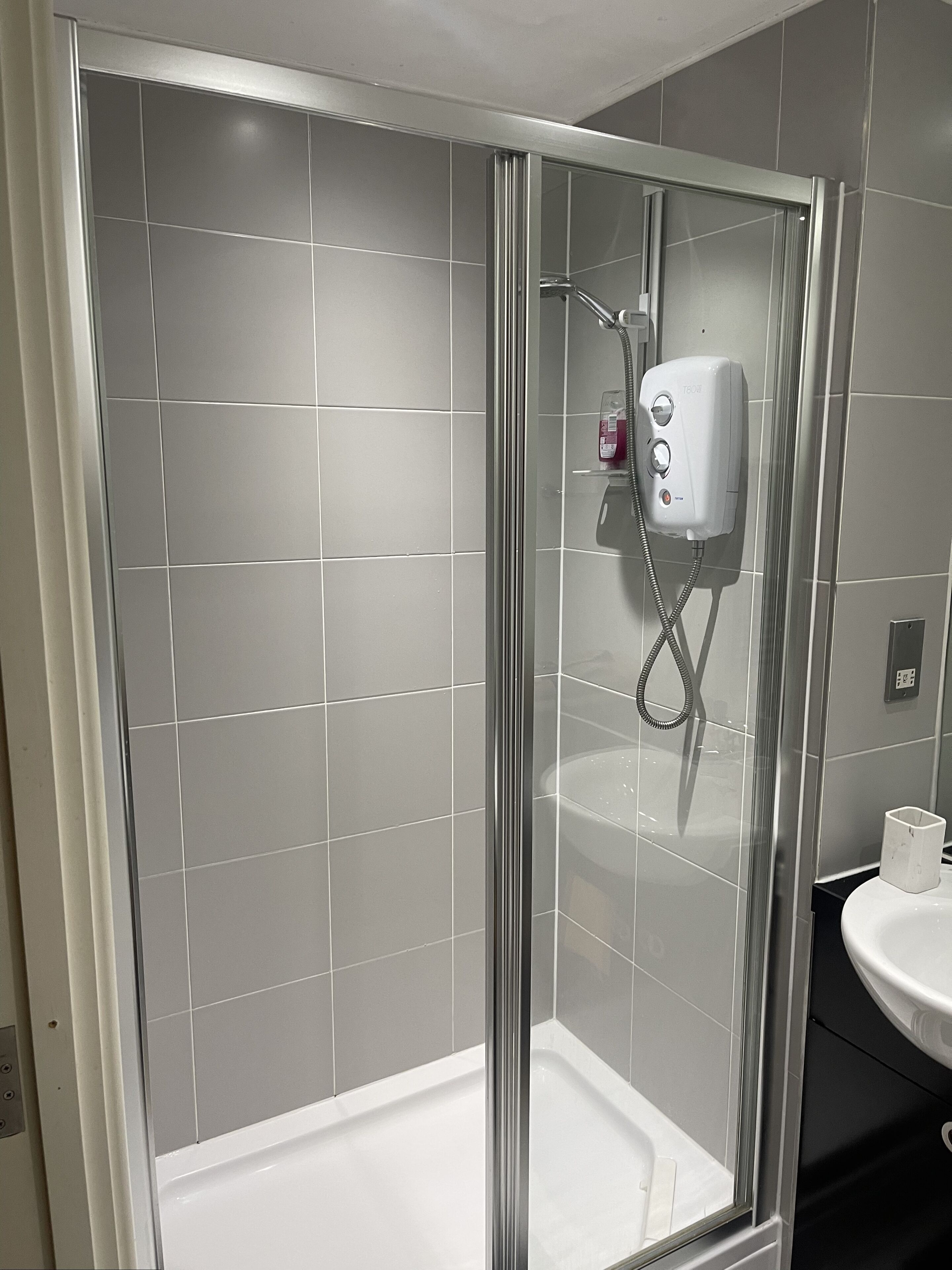 Une salle de bain moderne avec une douche à parois de verre, des murs recouverts de carreaux gris et un lavabo blanc.