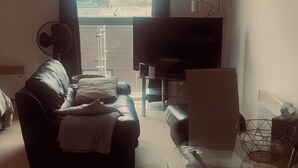 Een woonkamer met een bank, een glazen tafel, een stoel, een televisie en een raam met gordijnen.