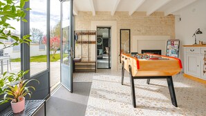 A room with a foosball table, a kitchen area, and a large window with a view of the outside.