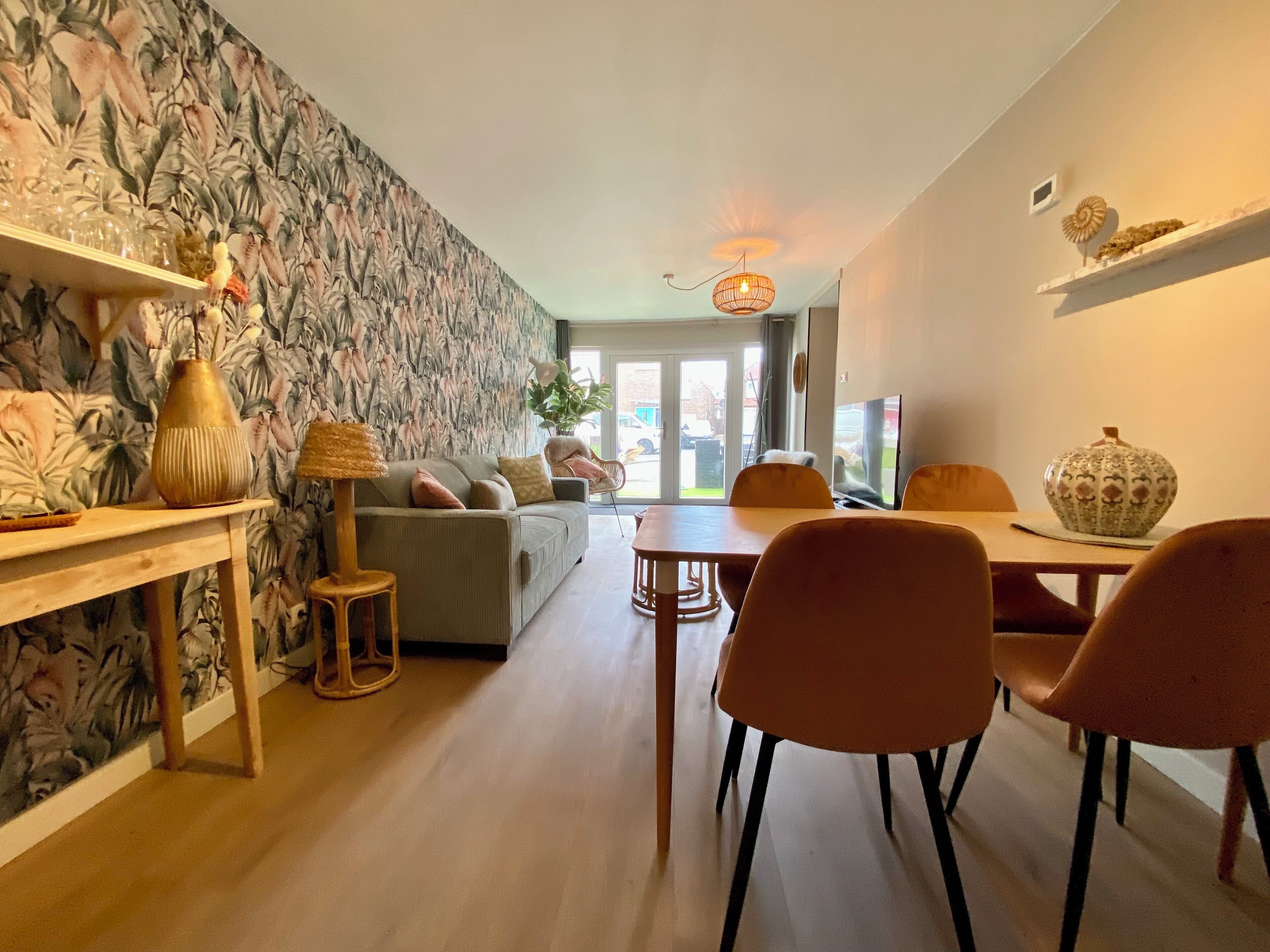 Un salon moderne avec un canapé, une table à manger et des chaises, un papier peint à motifs et une vue à travers une porte vitrée.