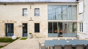 A stone building with a modern extension, a patio with a table and chairs, and a large window.