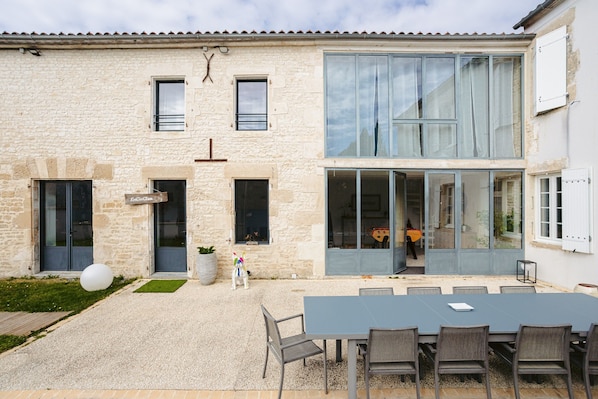 A stone building with a modern extension, a patio with a table and chairs, and a large window.