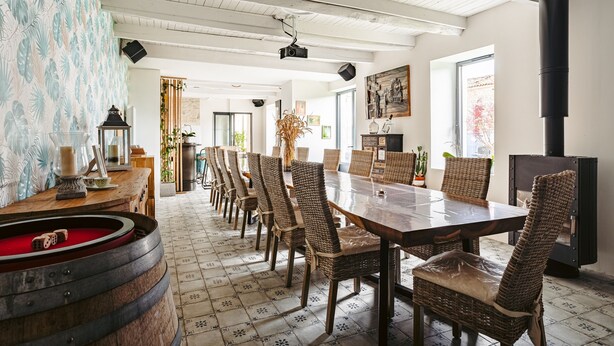 A dining area with a long table, wicker chairs, a wooden barrel, and a black stove.