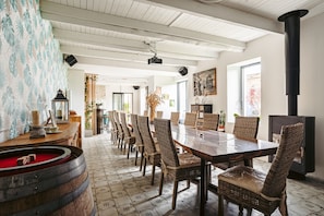 A dining area with a long table, wicker chairs, a wooden barrel, and a black stove.