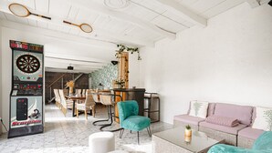 Un grand espace de vie comprenant un jeu de fléchettes, un canapé, une table basse et un coin repas avec des chaises et une table.