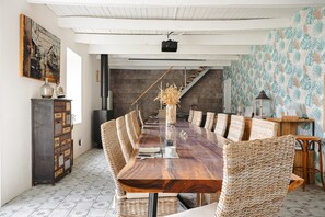 Ein Esszimmer mit einem langen Holztisch, Korbstühlen, einem Schrank und einer Treppe im Hintergrund.