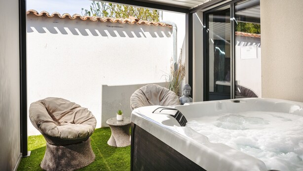Un bain à remous avec un coussin, une chaise en osier et une petite table agrémentée d’une plante.
