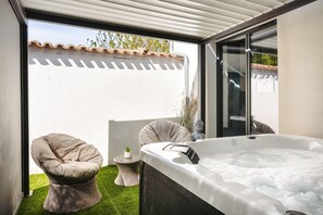 Ein Whirlpool mit Sitzkissen, ein Korbstuhl und ein kleiner Tisch mit einer Pflanze.
