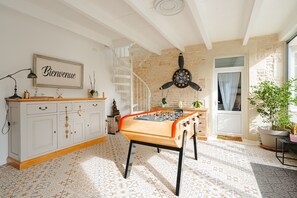 Una habitación con mesa de futbolín, una escalera, un reloj y un letrero de bienvenida.