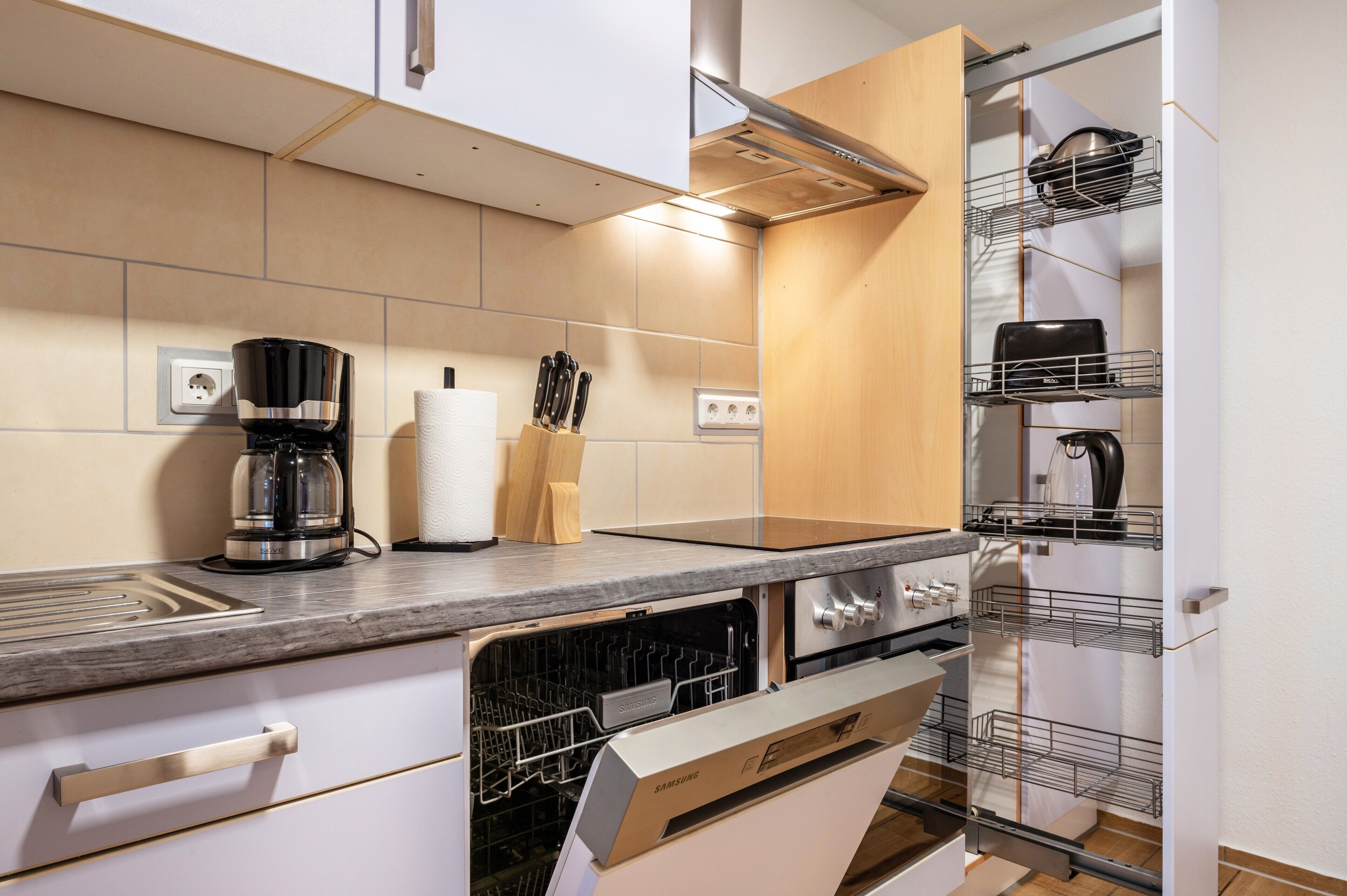 Eine moderne Küche mit Geschirrspüler, Backofen und Kaffeemaschine auf der Arbeitsplatte.