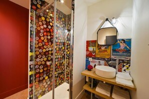 A bathroom with a wall of beer bottle caps, a round sink, a mirror, and various posters. - puits de jouvence (Bourges)