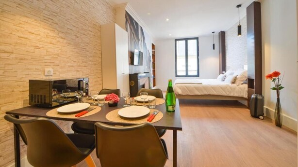 A modern living room with a dining area, a bed, and a large window. - puits de jouvence (Bourges)