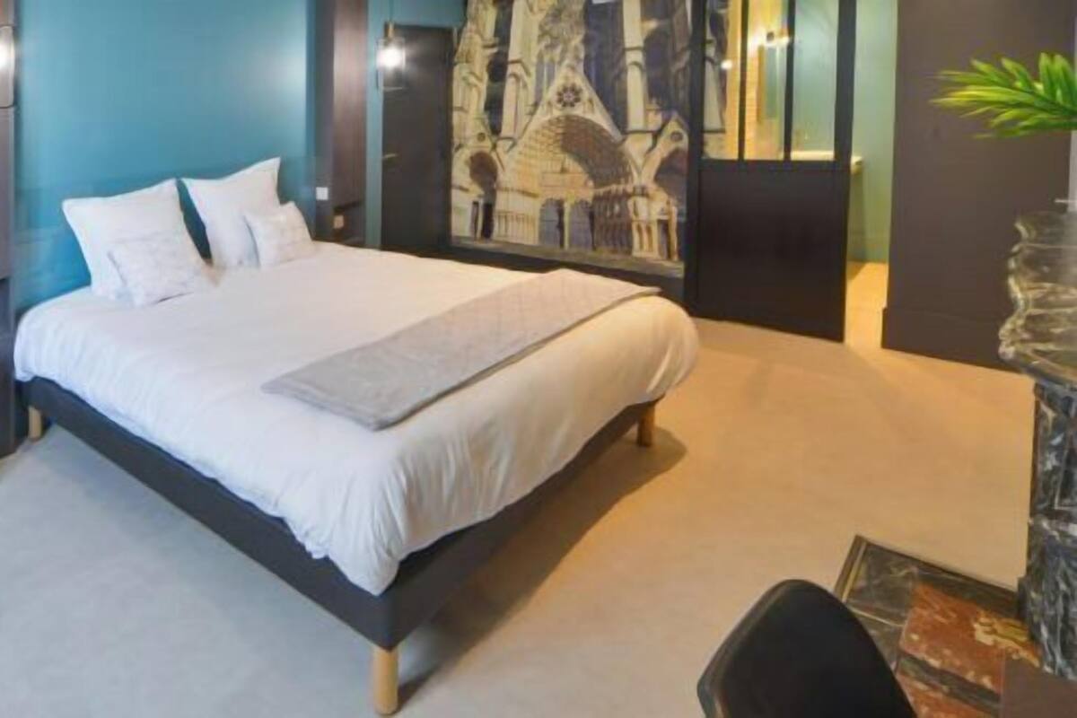 A modern bedroom with a large bed, a bedside table, a chair, and a wall-mounted artwork.