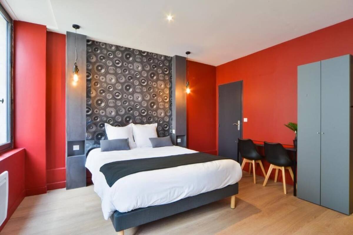 A modern bedroom with a large bed, a red accent wall, and a unique circular pattern wall.