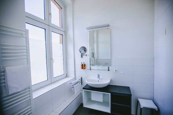 A modern bathroom with a white sink, mirror, and window. - Johanniter Hotel Wittenberg (Lutherstadt Wittenberg)